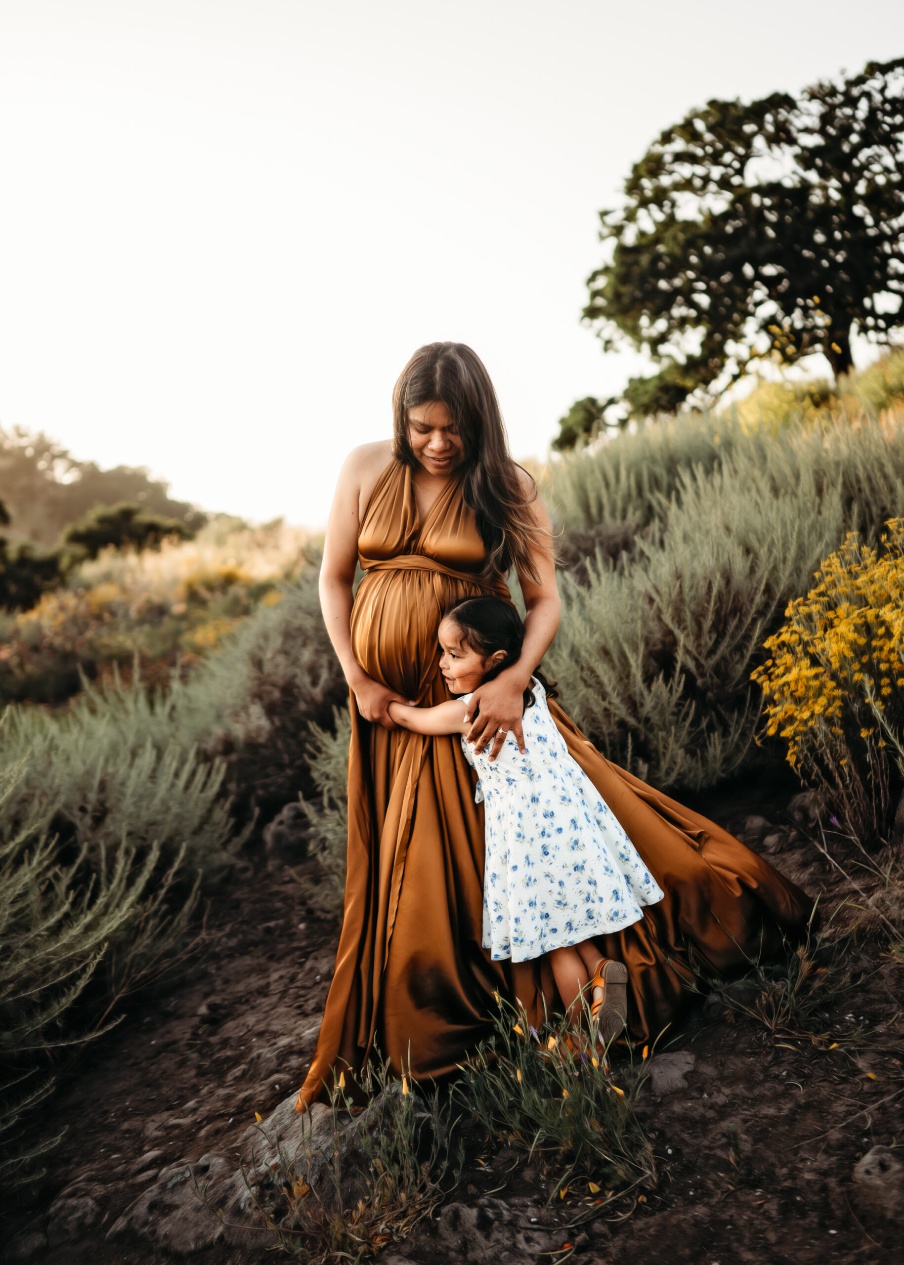Toddler hugs moms leg during her maternity photography session