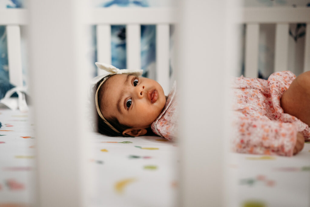 newborn baby looks through the side of her crib