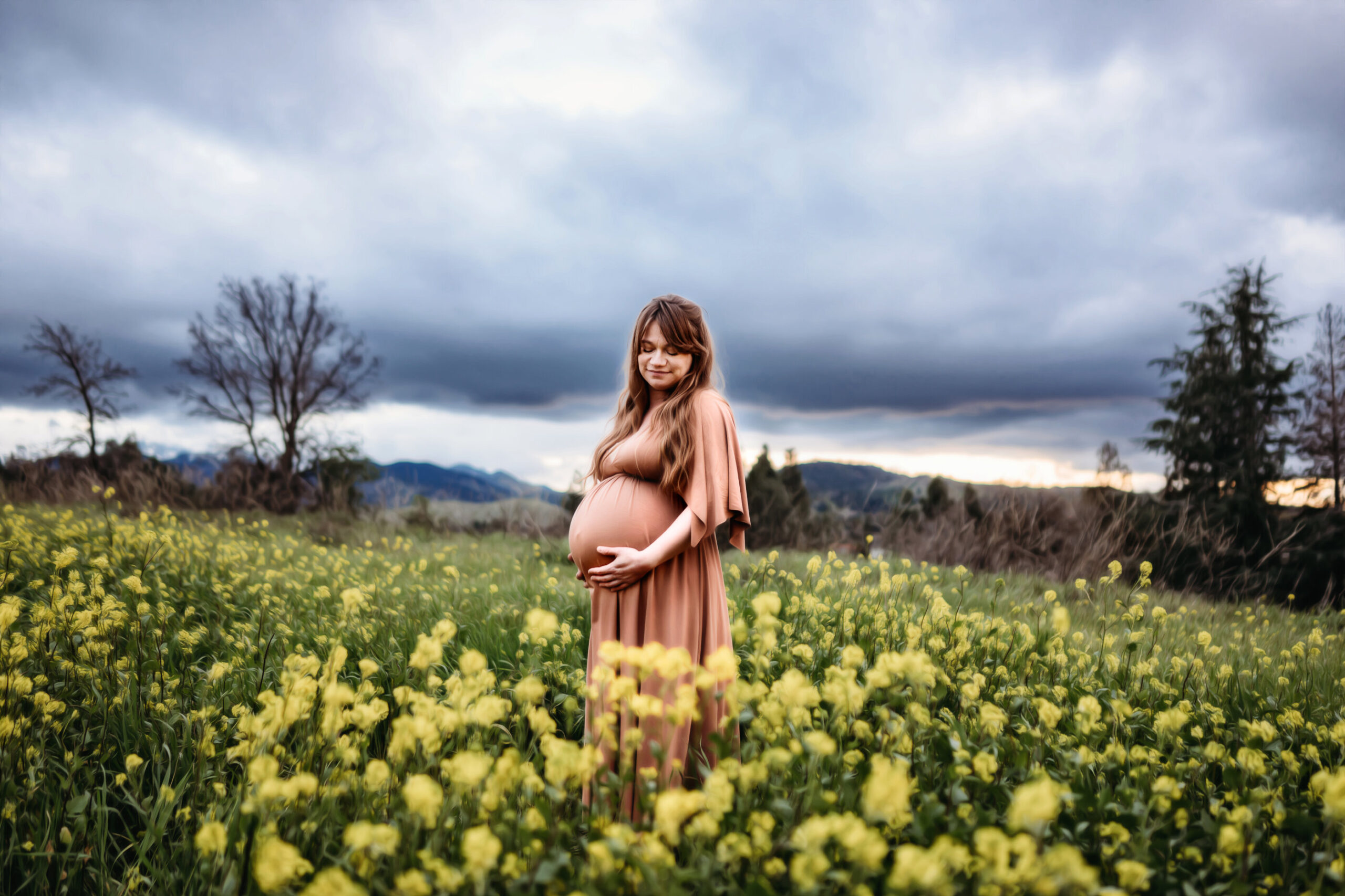 A spring maternity photography session with a mama in a field of wildflowers. She holds her belly and smiles softly. You can see the walnut creek open space behind her featuring mount diablo.