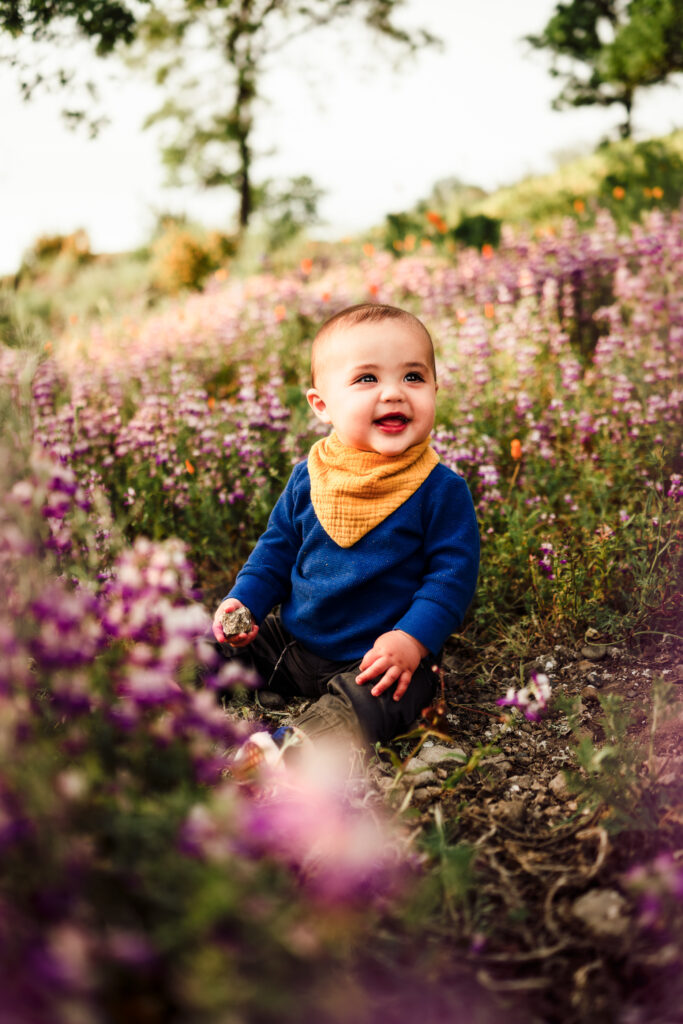 A baby sits smiling in a field of purple wildflowers