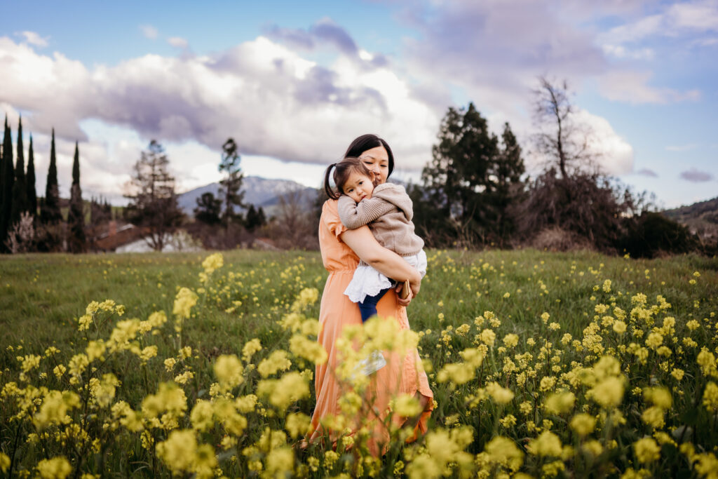 a mustard flower field at the base of mt diablo. a mom hold her toddler who calmly looks at the camera