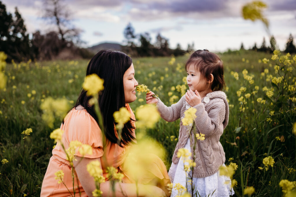 A toddler hold a bunch of mustard flowers out for her mom.