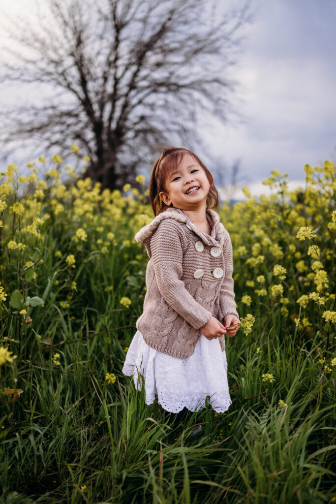 A toddler smiles at the camera, in her hand a bouquet of wildflowers.