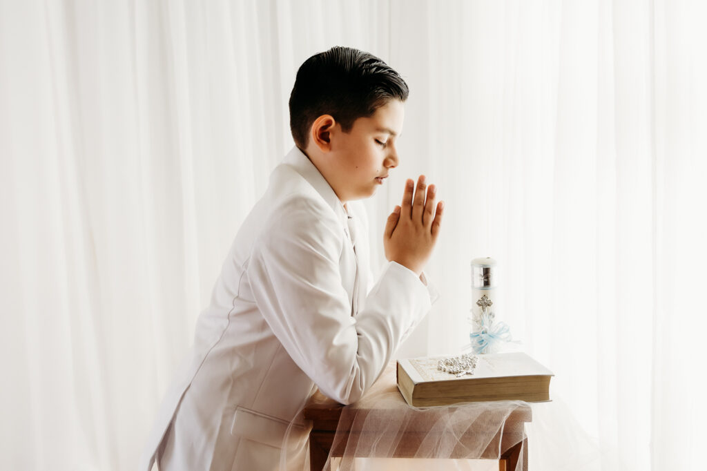 first communion photo of a boy praying. he has a family bible and his rosary