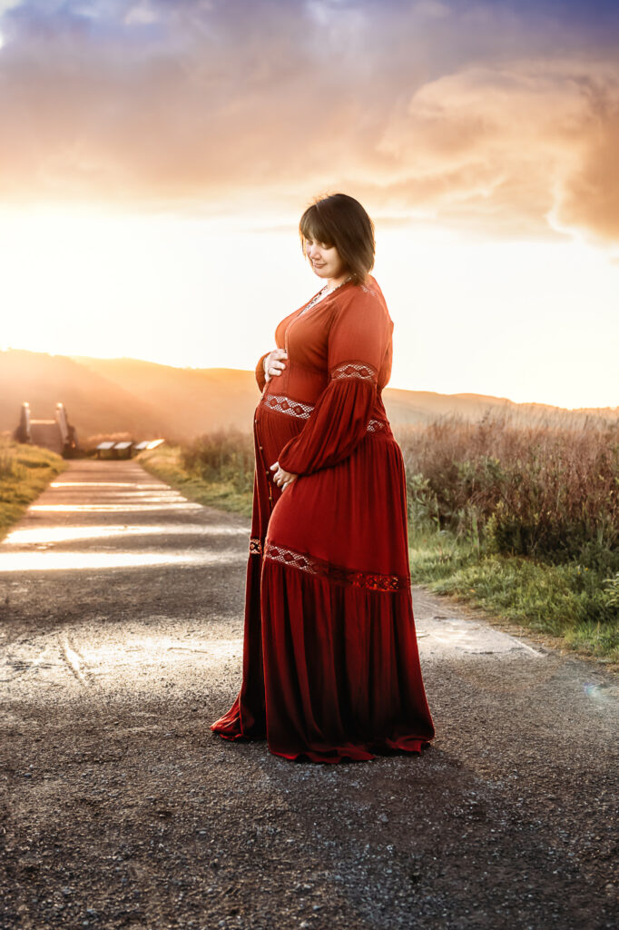 pregnant mama in red flowing maternity dress under a colorful sunset