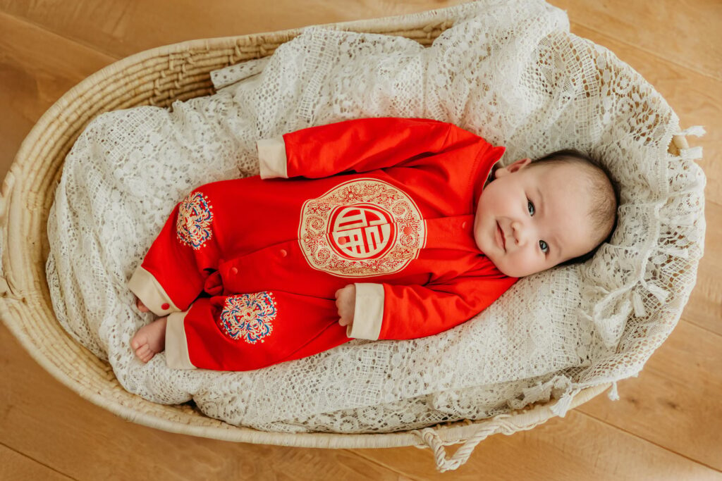 Baby girl smiling up at the camera wearing a traditional red outfit to celebrate her 100 days!