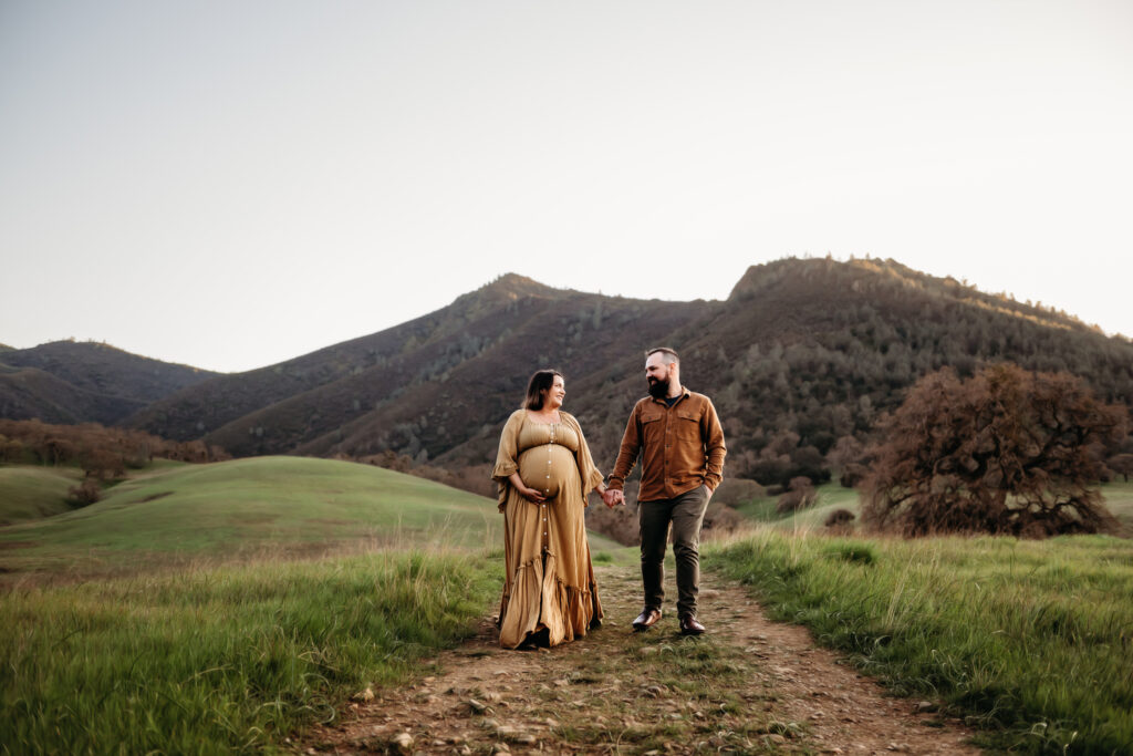 pregnant mama and her husband walking towards the camera. mt diablo is behind them.