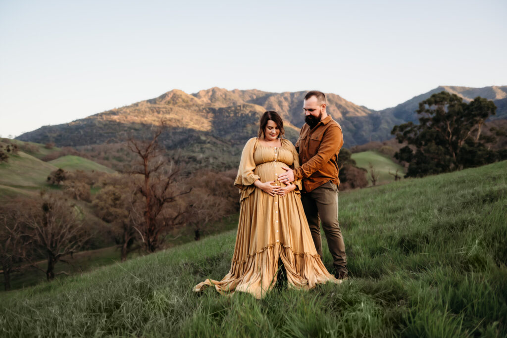 husband and wife smile and look down at the womans pregnant belly.