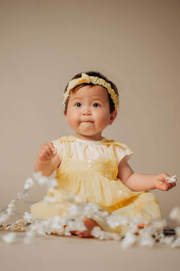 baby in yellow dress with cherry blossom branches around her. 