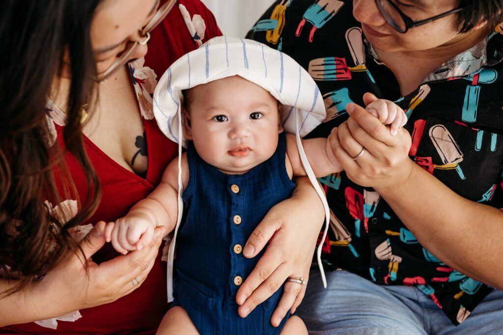 close up of baby on parents laps. baby has a blue romper and sun hat