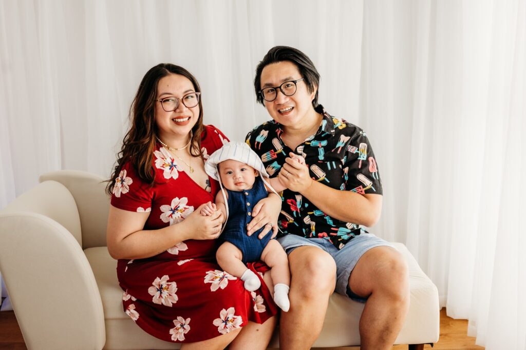 Family of 3 looking and smiling at camera during the 100 days photo shoot in studio