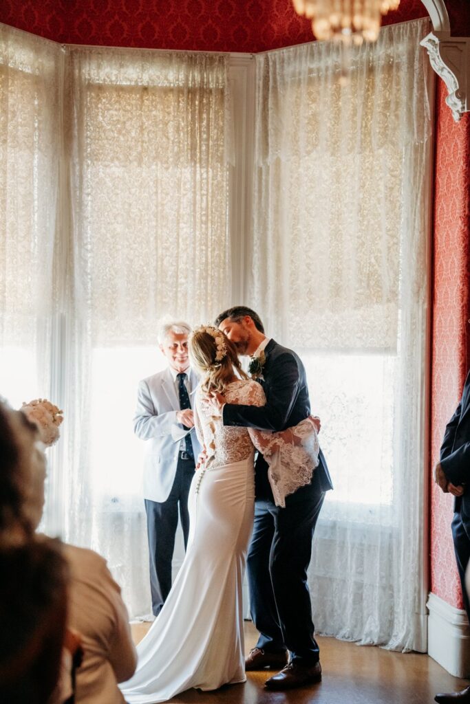 bride and grooms first kiss in front of the windows in the john muir house