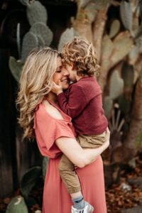 mom smiles as her son holds her face kissing her