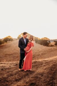 woman in peach maternity dress with her husband. they stand on the walnut creek open space trails