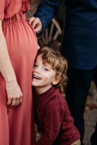 toddler smiles as he leans against his moms belly