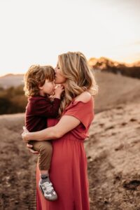 mom kisses toddlers forehead as he sucks his thumb, looking up at her