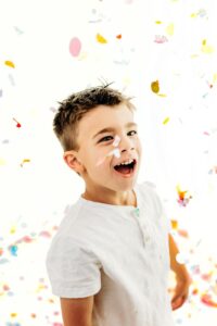 boy smiles up at confetti falling in photography studio
