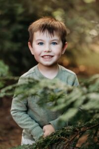 little boy smiles while hiding in redwood trees