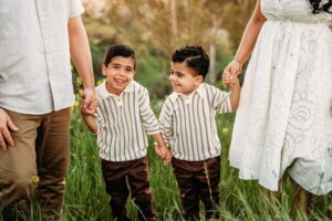 2 boys hold hands between their parents. both boys are smiling and being silly during their photography session