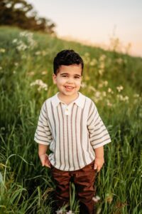 little boy smiles at camera mid laugh. there are flowers behind him.
