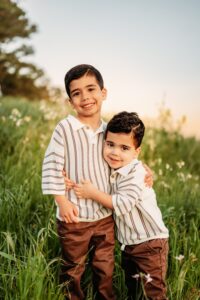 2 brothers hugging smiling at camera - the flower field is behind them.
