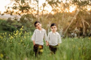 brothers hold hands in matching outfits. yellow flowers are blooming on the hill behind them.