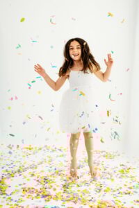 girl jumps around in rainbow confetti