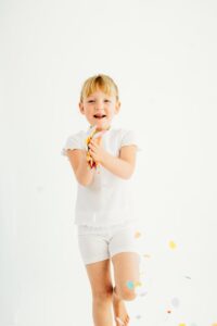 girl in all white throws rainbow confetti pieces