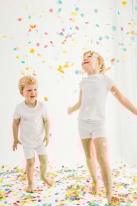 siblings look up at confetti and jump around the photography studio