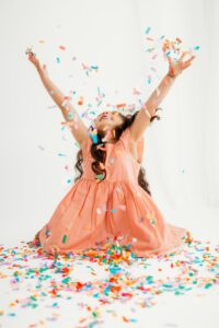 girl in pink dress throws confetti and leans back