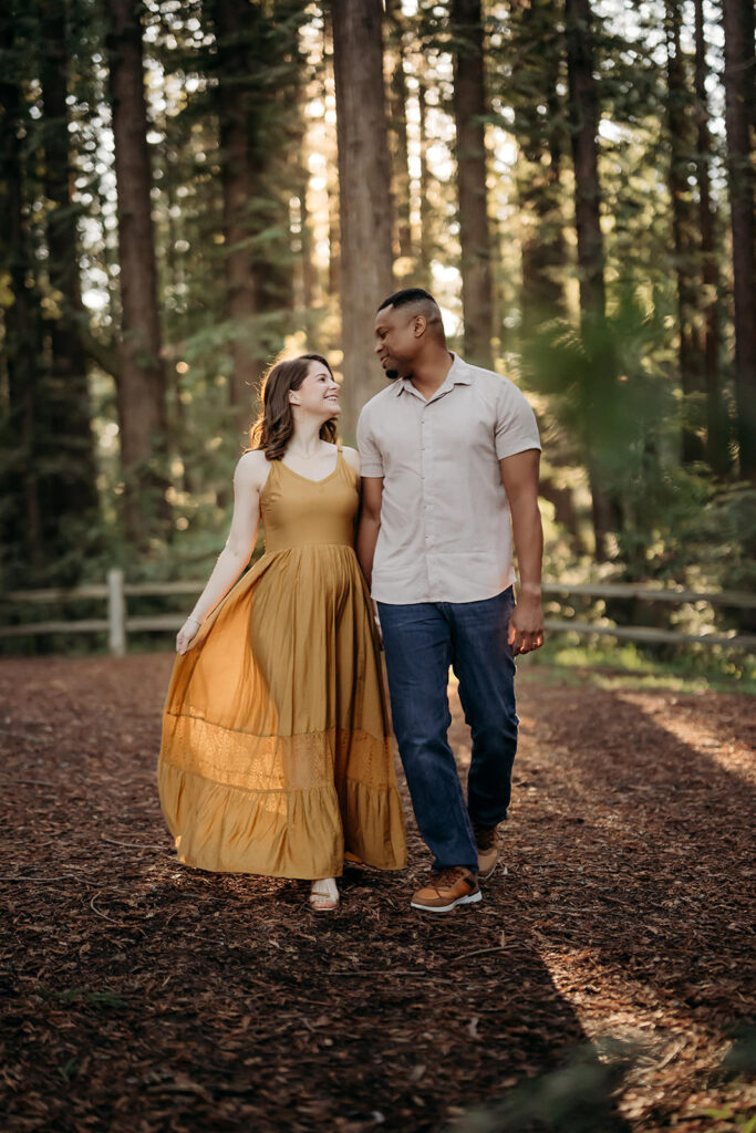 Couple walking hand in hand along a redwood forest path during a relaxed maternity session in the East Bay.