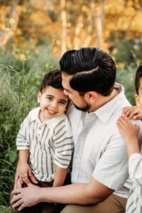a boy on his dads lap. boy smiles at camera