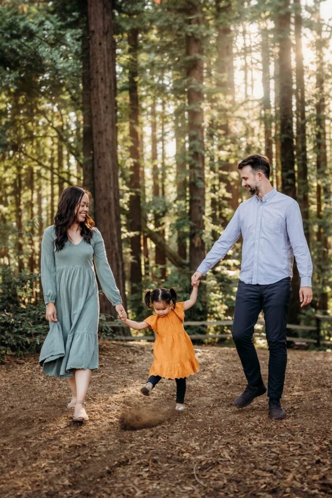 Parents walking hand in hand with their child along a forest path during an outdoor family photography session in lamorinda area