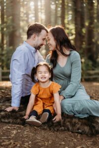 family of 3 sitting on a blanket. the toddler looks at the camera smiling