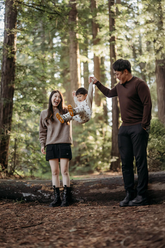 parents hold their toddlers hands as he jumps off a redwood log