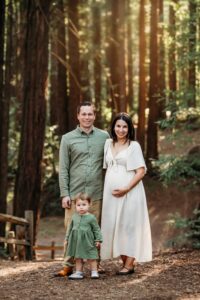 family of 3 smiling at camera in a forest