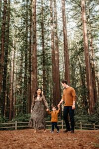 mom dad and toddler walking through a redwood forest