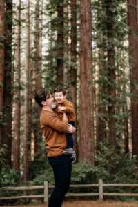 dad lifts his son in a massive redwood forest