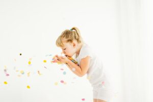 side view of little girl blowing rainbow confetti around a photography studio