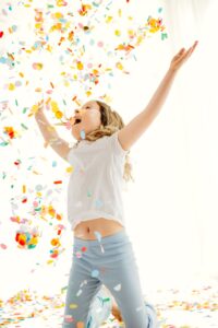 little girl tossing confetti while on her knees. her mouth is open and hands are up celebrating