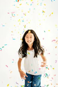 girl smiling as multi colored confetti falls around her.