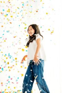 big sister stands and smiles watching confetti fall