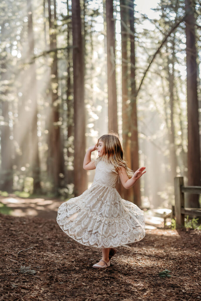 little girl in lace dress twirls among the redwoods