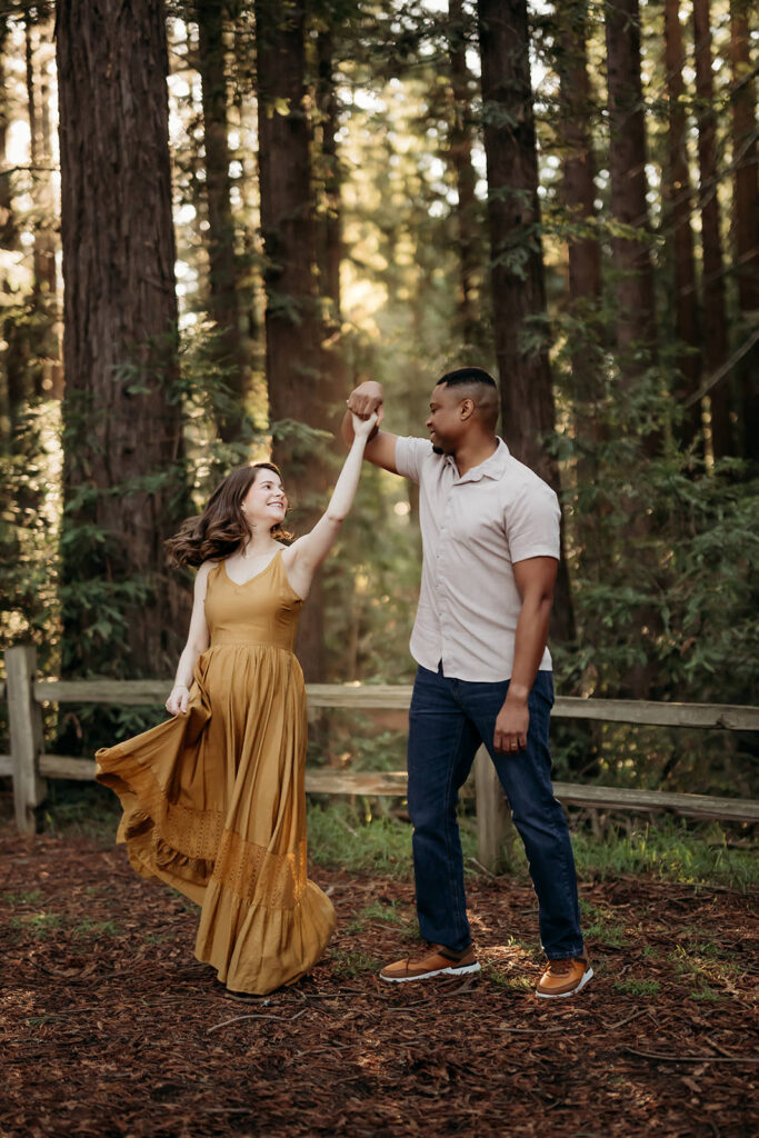 Couple twirling together on a forest path, laughing and moving naturally during an intimate maternity session near Walnut Creek.