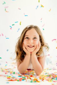 girl looks up as confetti falls around her. her head is supported by her hands