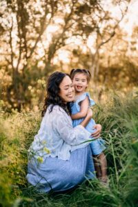 toddler smiles at camera and mama gives her a big hug