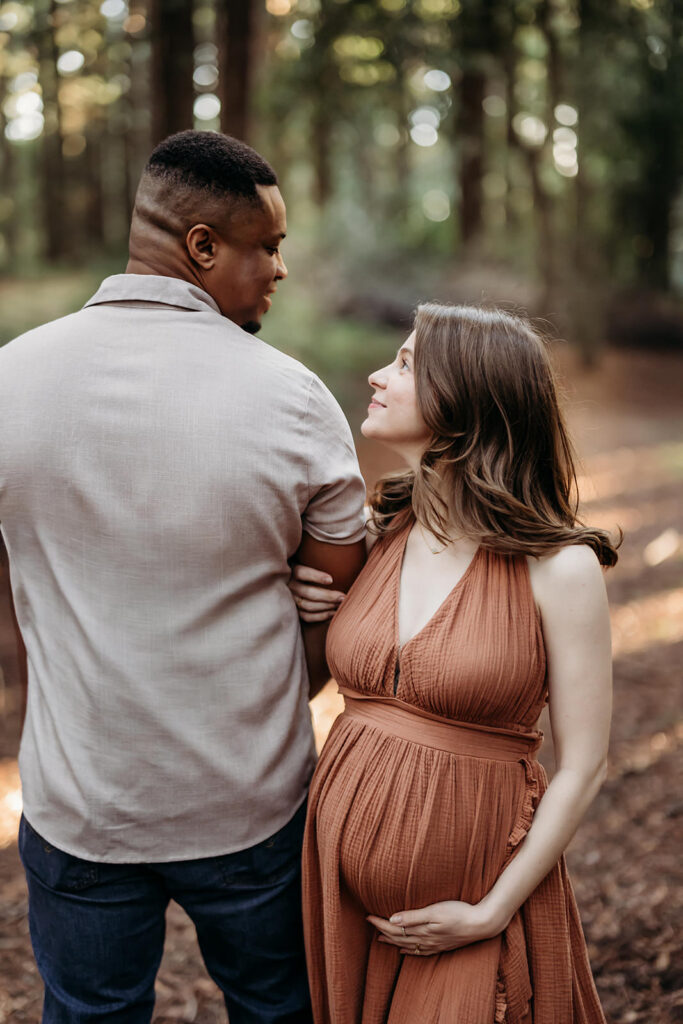 Expectant parents paused on a sunlit trail, exchanging a soft look while holding their growing belly during an East Bay maternity session.