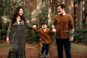 toddler balances on a redwood log while holding his parents hands