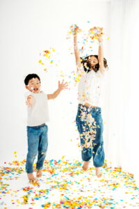 2 kids jumping and tossing confetti in white photography studio