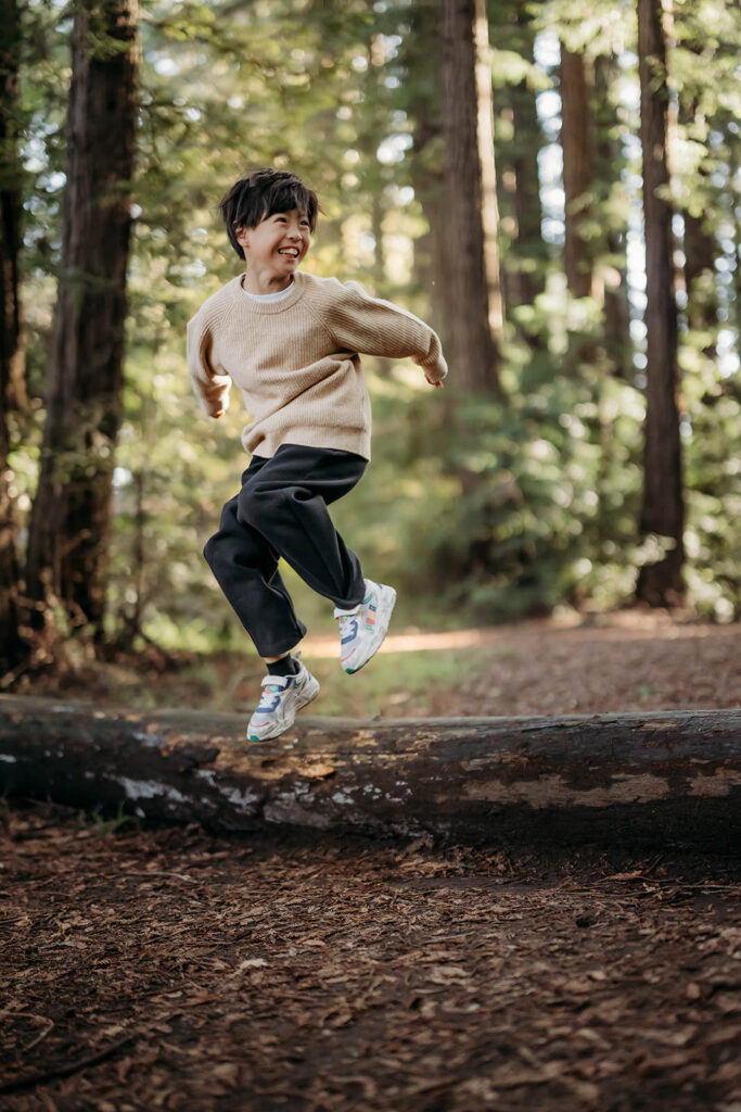 boy jumping off a redwood log looking over his shoulder